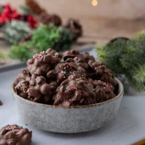 Bowl of crockpot candy chocolate peanut clusters topped with red, green, and white sprinkles for an easy holiday treat.