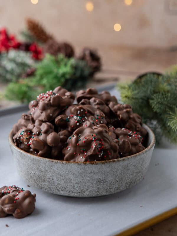 Bowl of crockpot candy chocolate peanut clusters topped with red, green, and white sprinkles for an easy holiday treat.