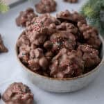 Bowl of chocolate crockpot candy peanut clusters topped with Christmas sprinkles.