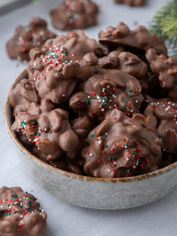 Bowl of chocolate crockpot candy peanut clusters topped with Christmas sprinkles.