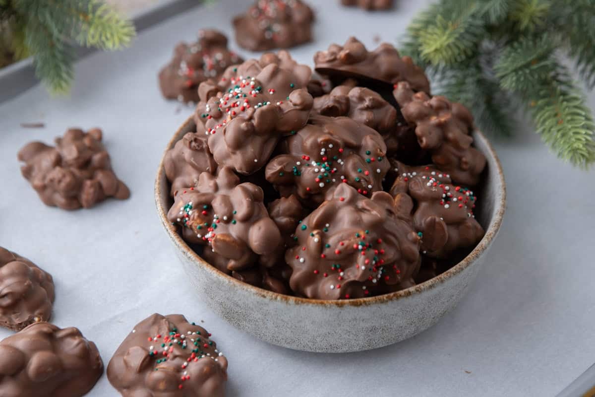 Bowl of chocolate crockpot candy peanut clusters topped with Christmas sprinkles