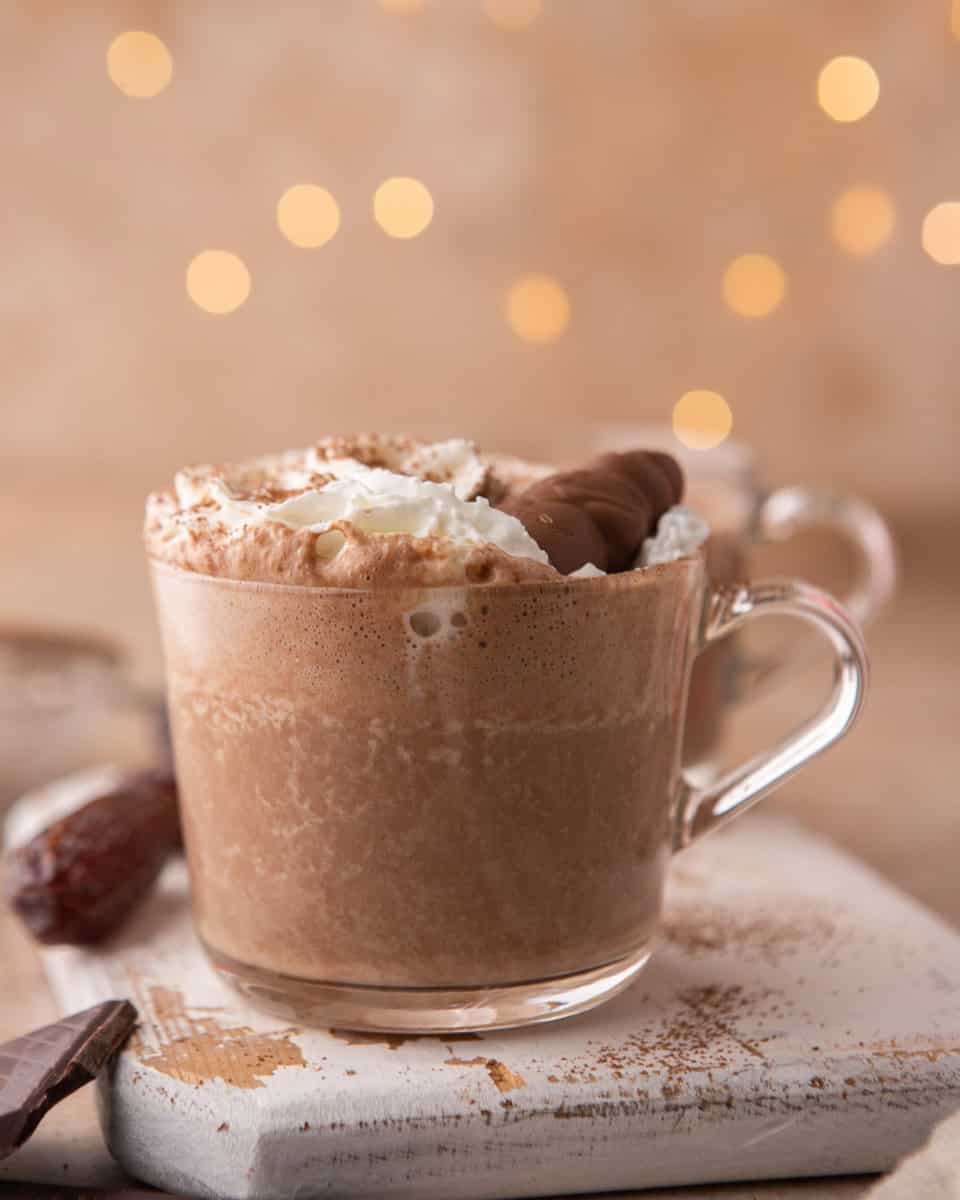 Date sweetened hot chocolate in a glass mug topped with whipped cream
