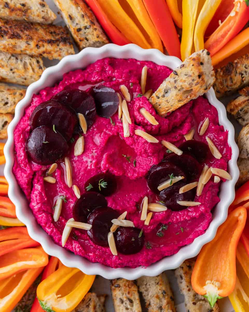 Beet hummus served in a bowl with crostini and fresh vegetables