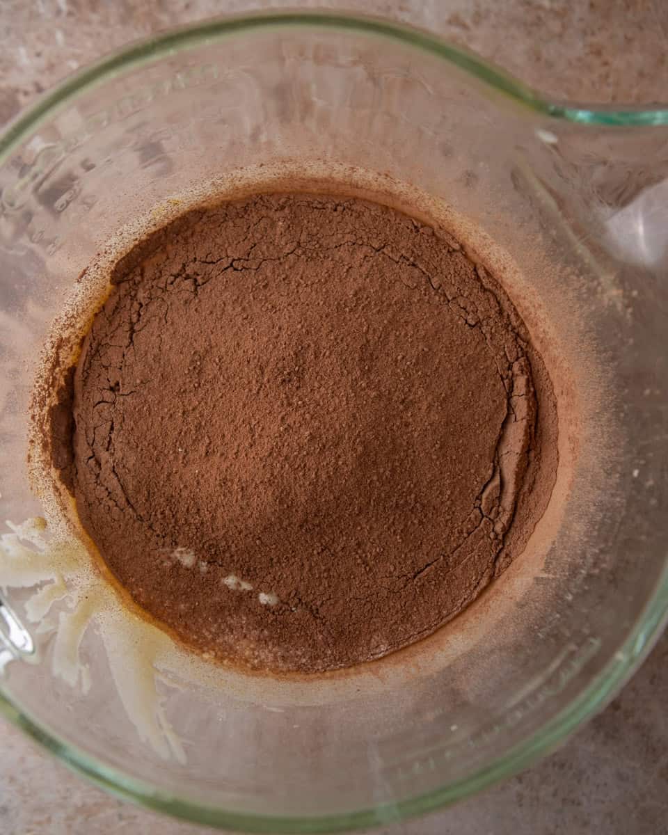 Cocoa powder and flour added to brownie pudding batter in a glass bowl
