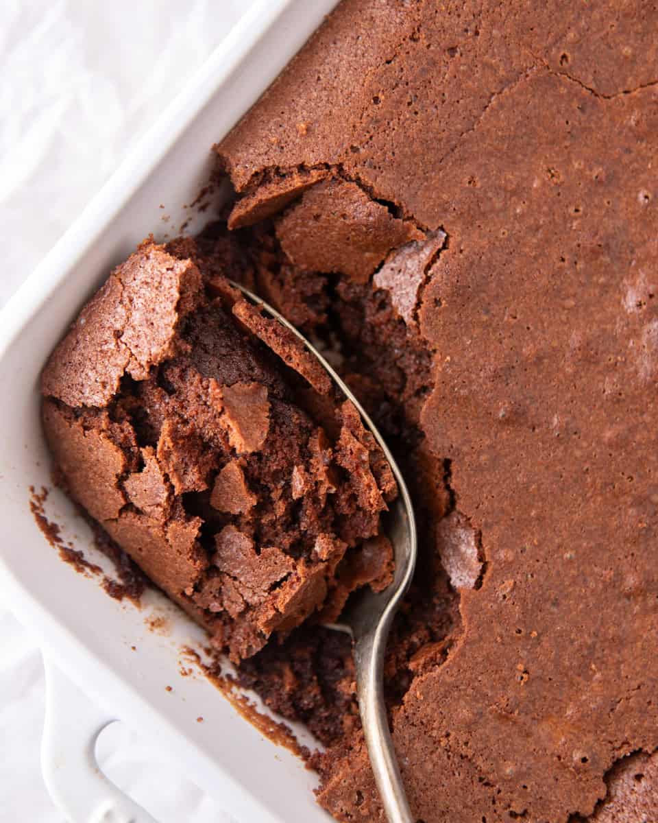 Ina Garten brownie pudding in a white baking dish with a spoon scooping out the fudgy spoonable center underneath the chewy brownie top