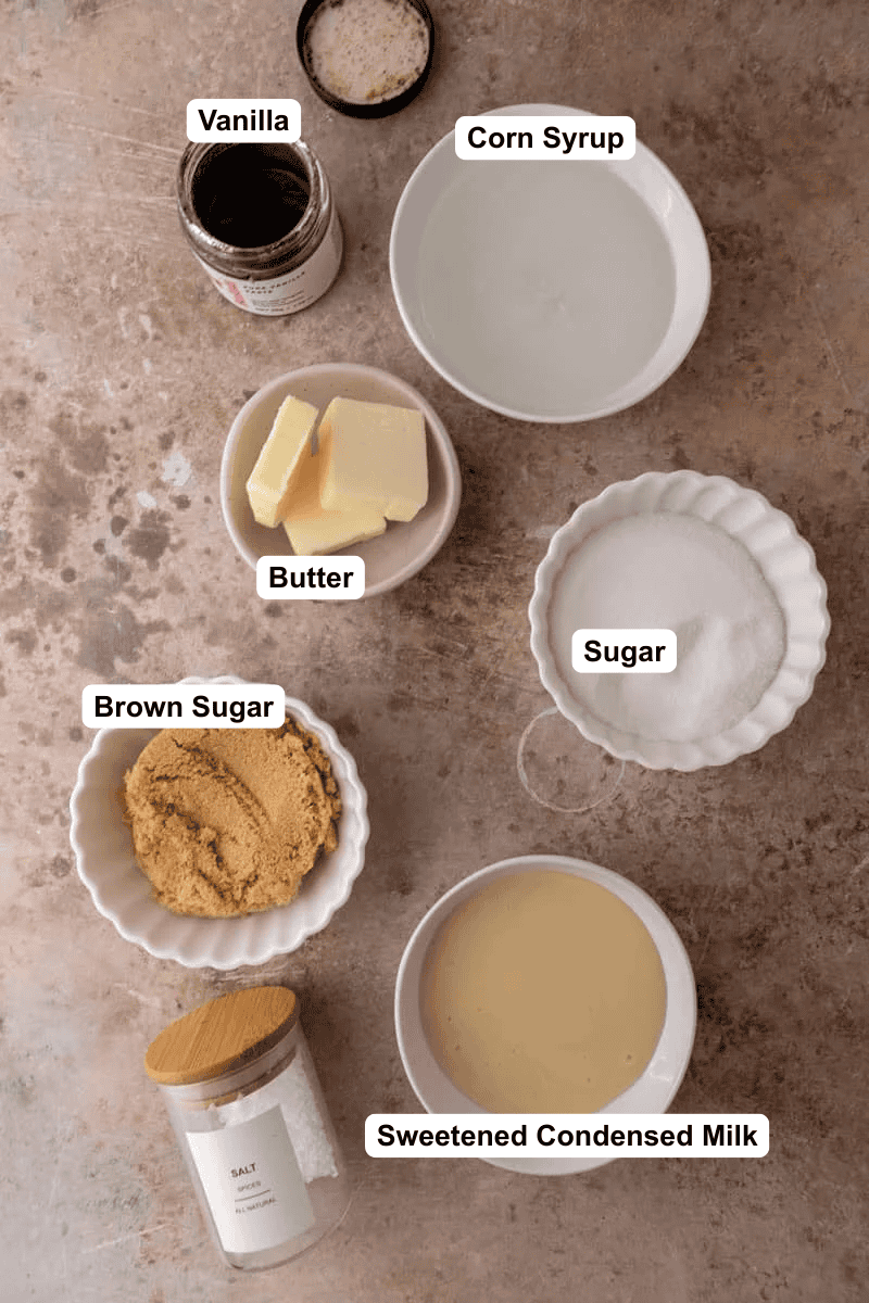 Ingredients for microwave caramels in small bowls: sweetened condensed milk, white sugar, brown sugar, butter, corn syrup, vanilla bean paste, and salt.