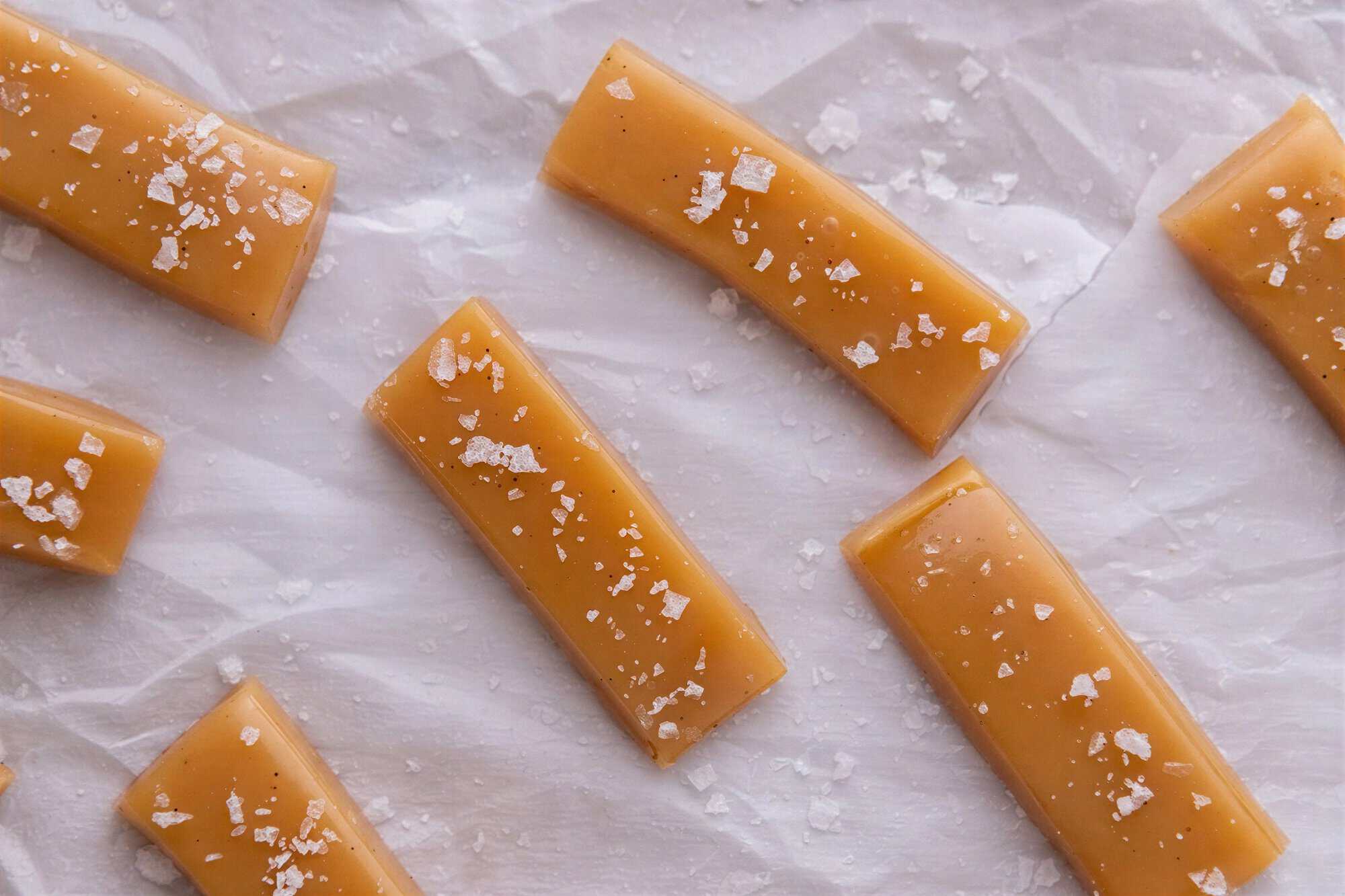 Strips of soft homemade microwave caramel topped with flaky sea salt on parchment paper.