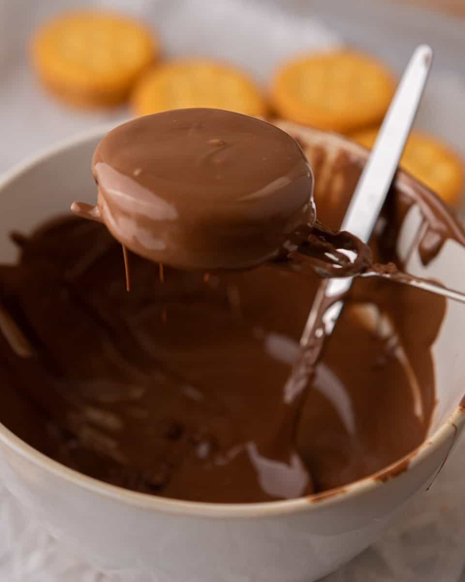 Ritz peanut butter cookies being dipped into melted milk chocolate