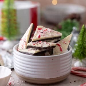Peppermint bark pieces stacked in a white bowl, topped with crushed candy canes.