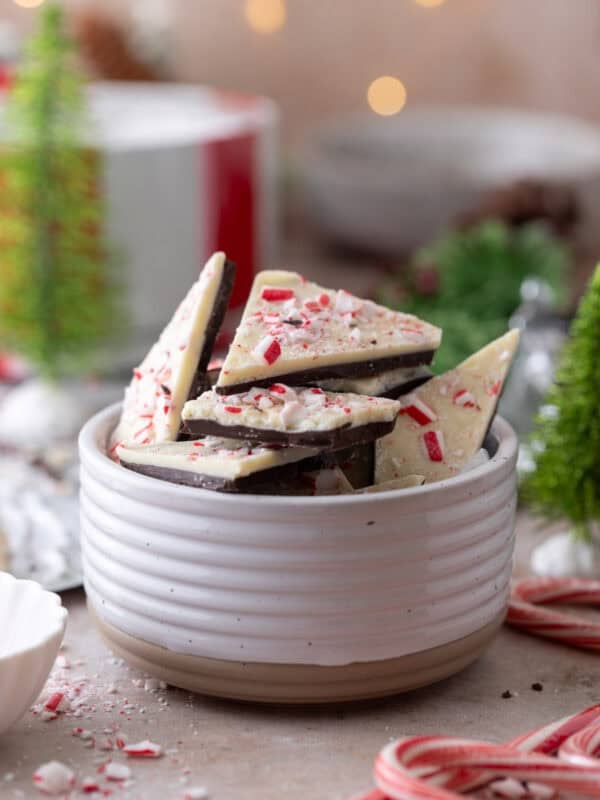 Peppermint bark pieces stacked in a white bowl, topped with crushed candy canes.