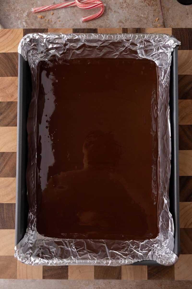 A baking pan lined with foil and filled with melted dark chocolate spread evenly.