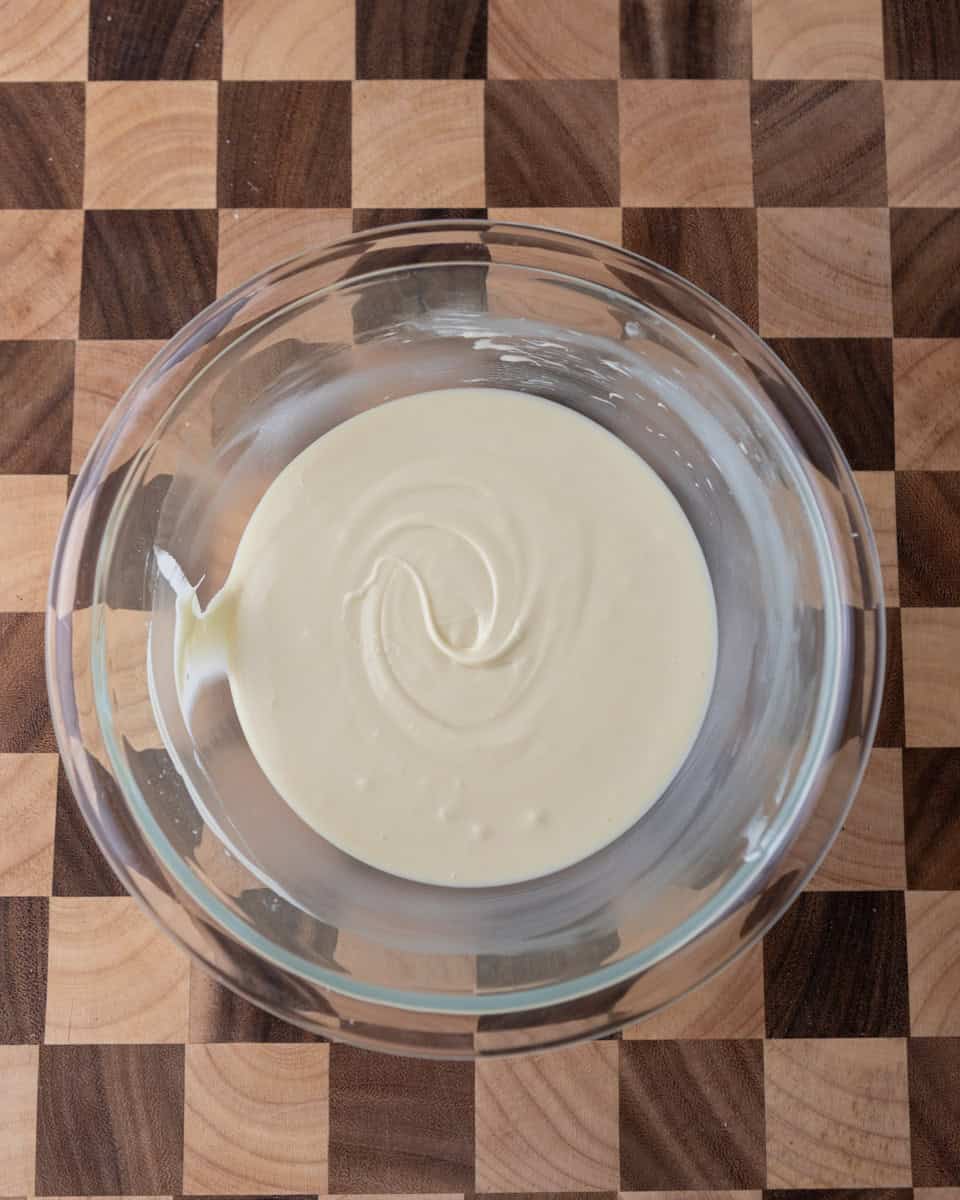 Melted white chocolate swirled in a glass bowl on a wooden board.