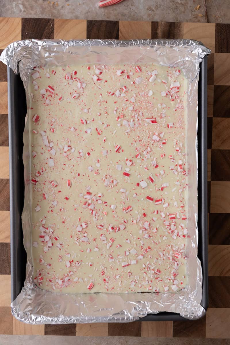 Peppermint bark topped with crushed candy canes in a baking pan before chilling.