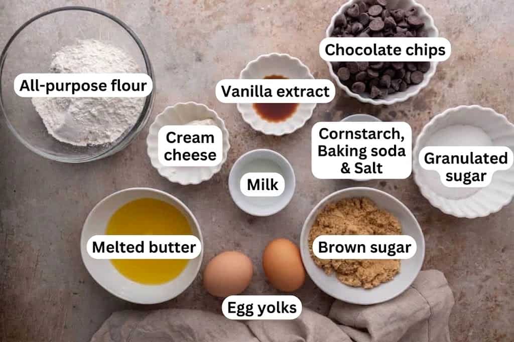 Ingredients for cream cheese chocolate chip cookies, including melted butter, eggs, and chips, in small bowls.