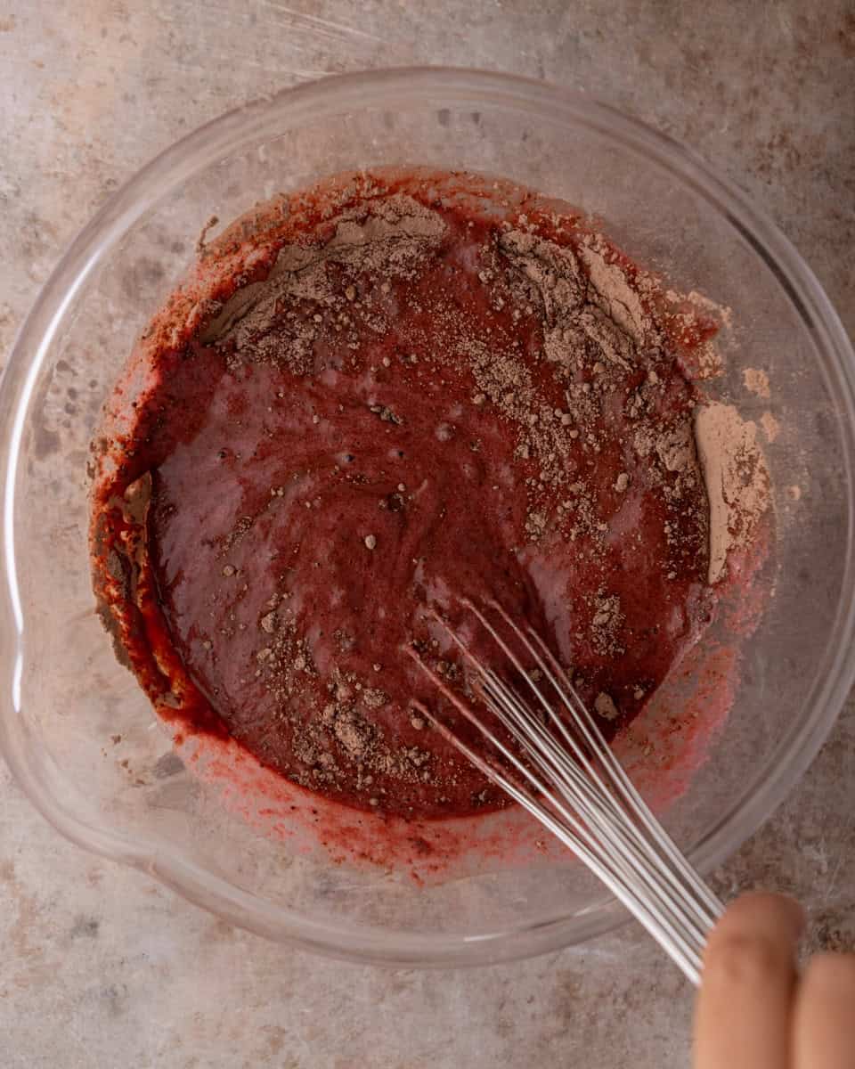 Dry chocolate cake ingredients being added to beet mixture in a bowl
