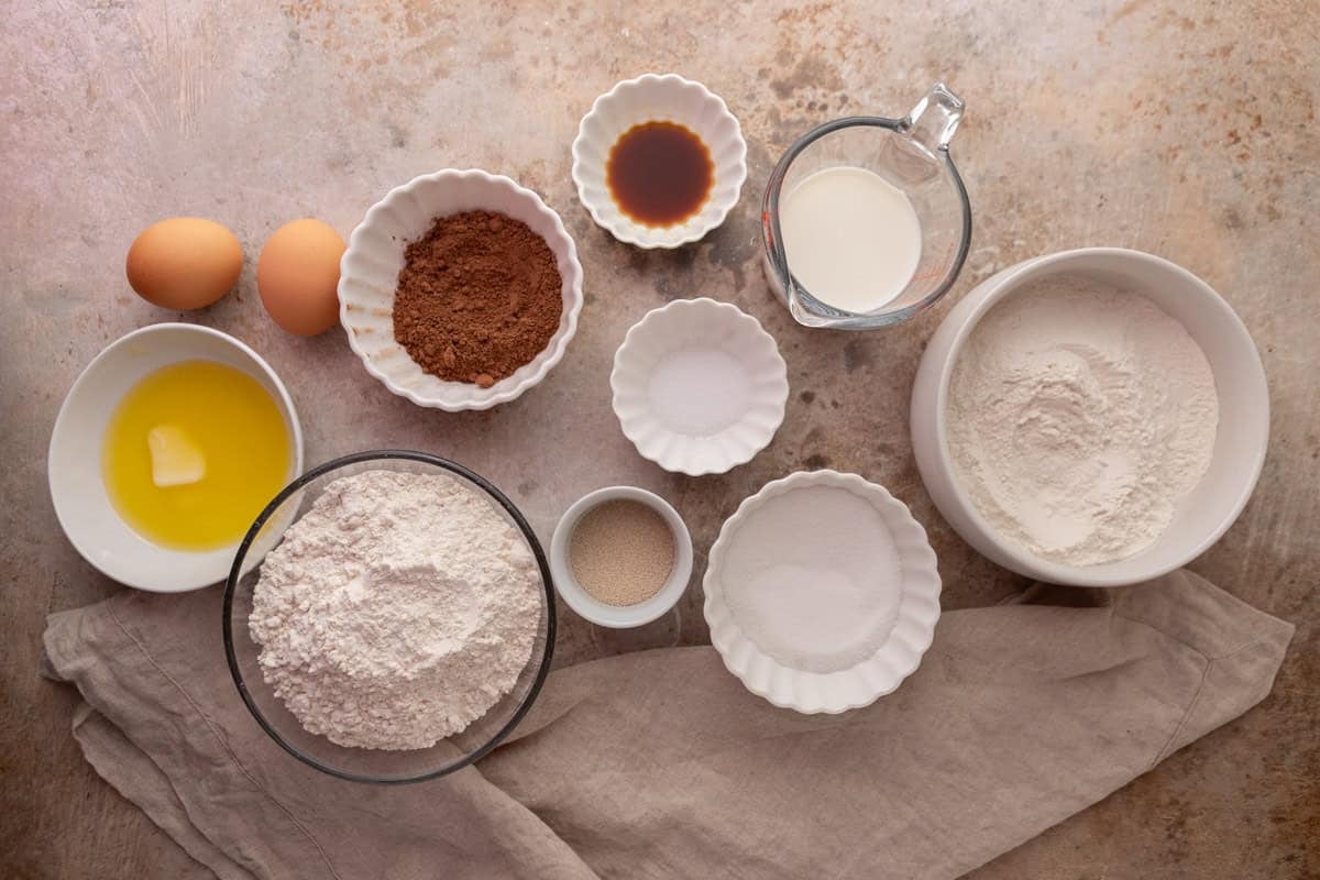 Ingredients for chocolate cinnamon roll dough including flour, cocoa powder, eggs, milk, and yeast