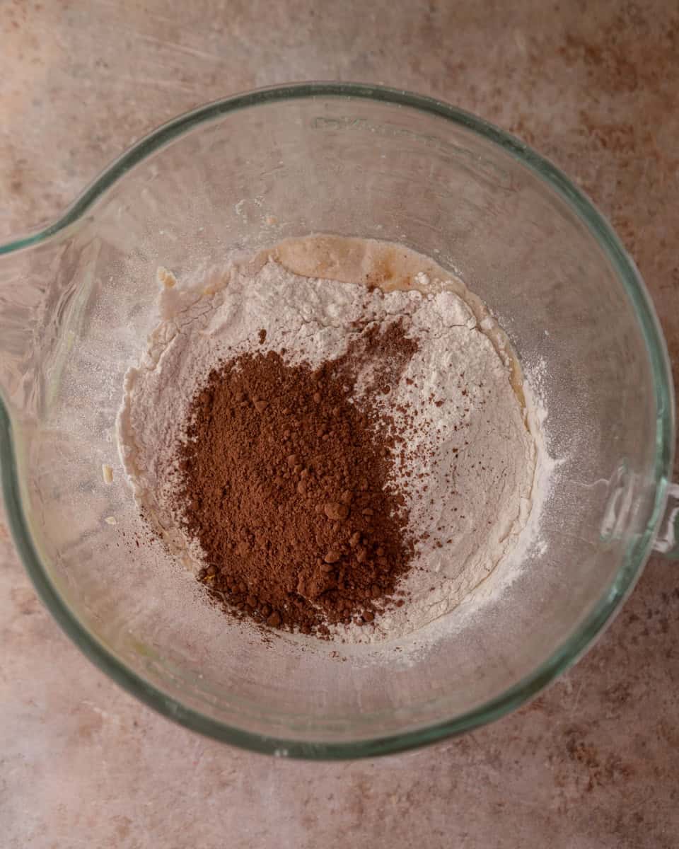 Flour and cocoa powder added to wet ingredients in a mixing bowl.