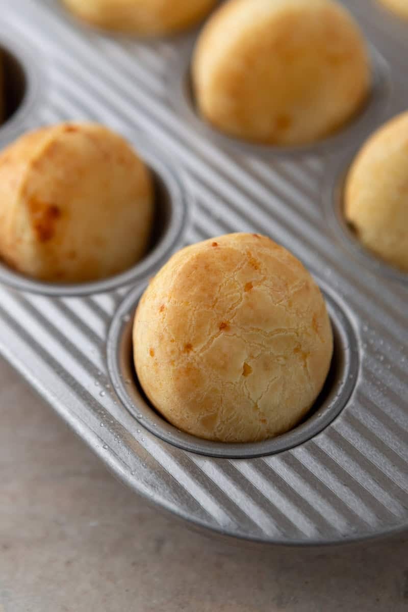Mini muffin cups filled halfway with Brazilian cheese bread batter, ready to bake and puff in the oven.