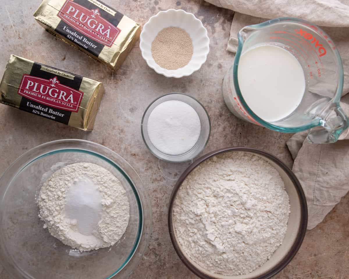 Ingredients for croissant cinnamon rolls including flour, milk, sugar, yeast, and European-style butter for lamination.