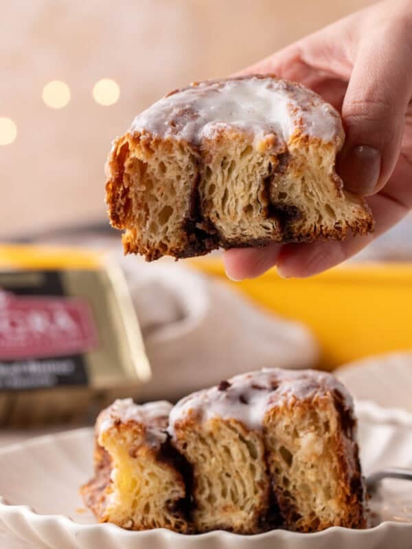 Hand holding a croissant cinnamon roll showing flaky laminated layers and cinnamon filling