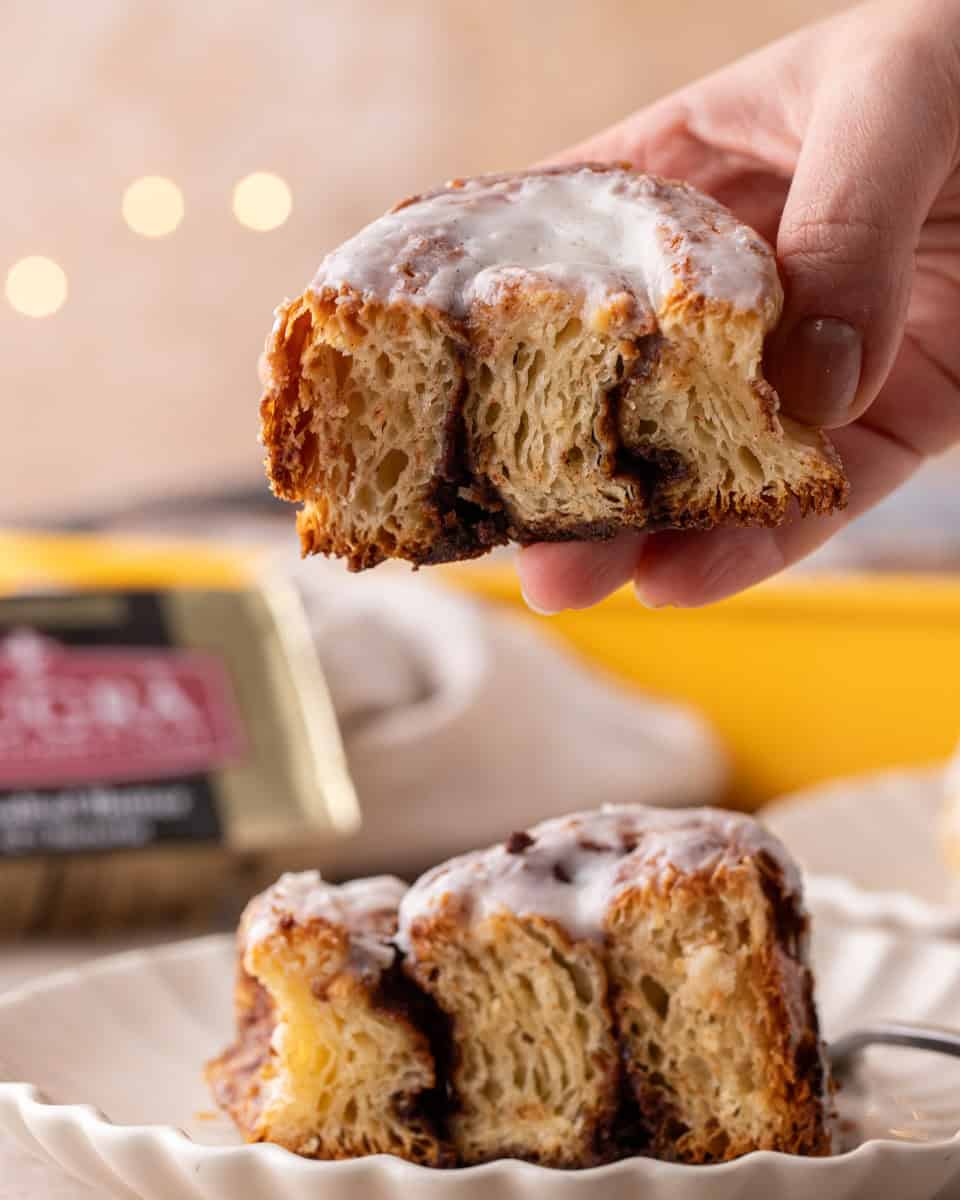 Hand holding a croissant cinnamon roll showing flaky laminated layers and cinnamon filling