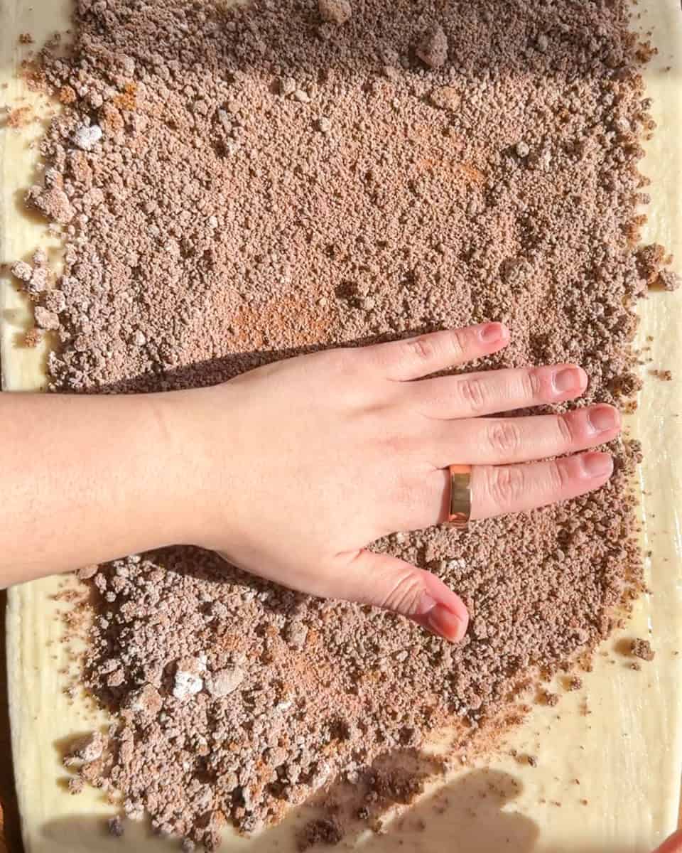 Hand spreading cinnamon sugar filling evenly over rolled croissant dough