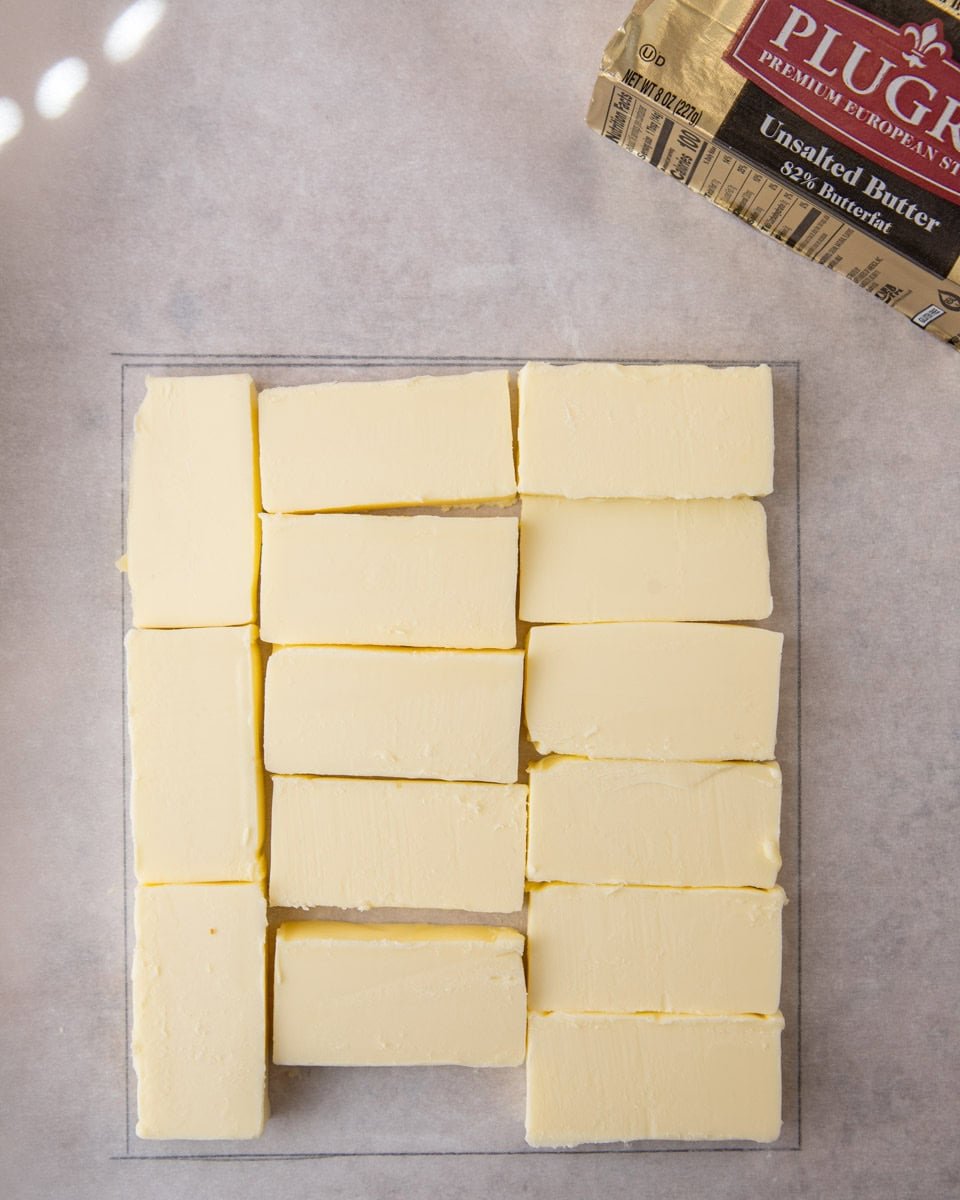 Cold butter sticks arranged on parchment inside a drawn square guide for lamination