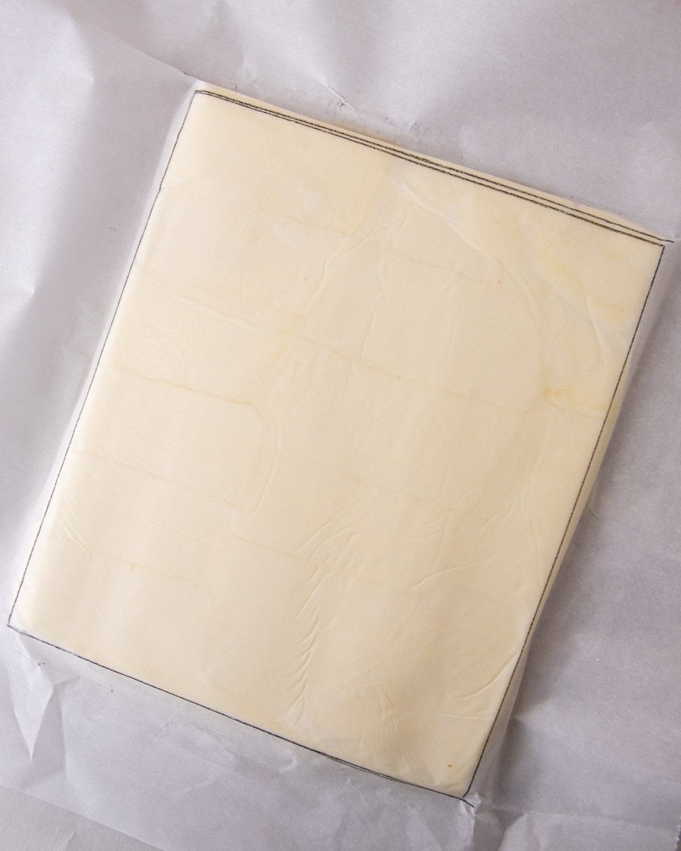 Butter pressed into a smooth square block inside parchment paper for laminating dough