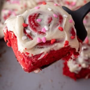 Soft red velvet cinnamon roll lifted from the pan showing the fluffy texture