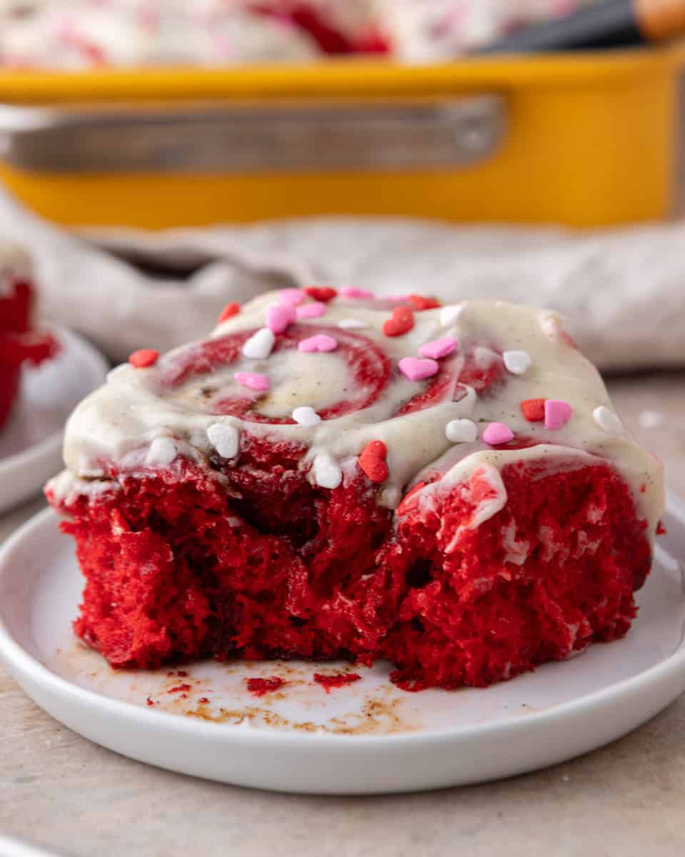 Red velvet cinnamon roll with cream cheese frosting and heart sprinkles on a plate