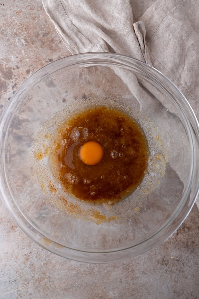 A room temperature egg added to the brown butter and sugar mixture in a glass bowl for a chocolate chip pizookie