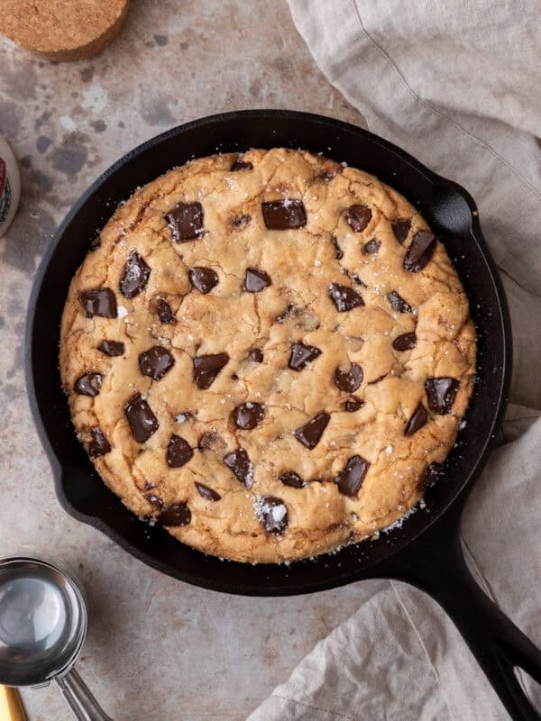 Overhead view of a freshly baked brown butter skillet cookie with golden edges, melted chocolate chunks, and flaky salt in an 8-inch cast iron pan