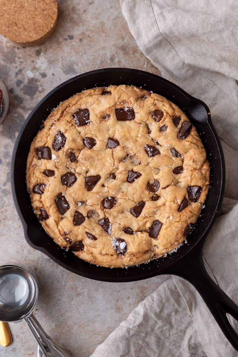 Overhead view of a freshly baked brown butter skillet cookie with golden edges, melted chocolate chunks, and flaky salt in an 8-inch cast iron pan