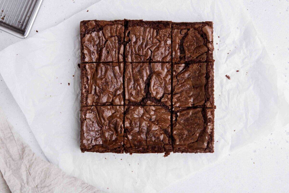 Overhead shot of upgraded boxed brownies sliced into nine squares on parchment paper showing shiny crinkly tops and fudgy texture