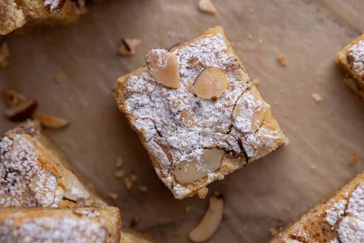 Almond croissant blondie bar topped with sliced almonds and powdered sugar on parchment paper showing the frangipane filling inside