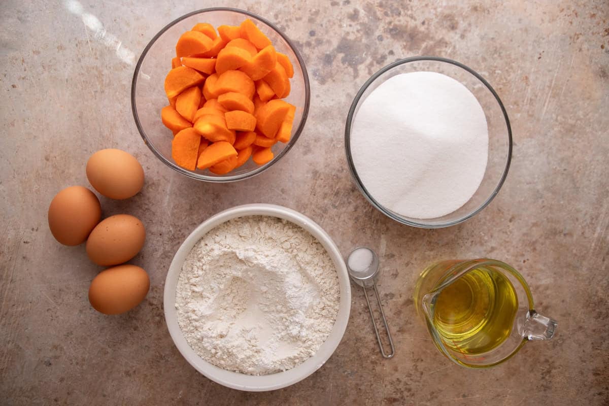 Ingredients for the cake batter including chopped carrots, eggs, flour, sugar, oil, and salt measured in bowls