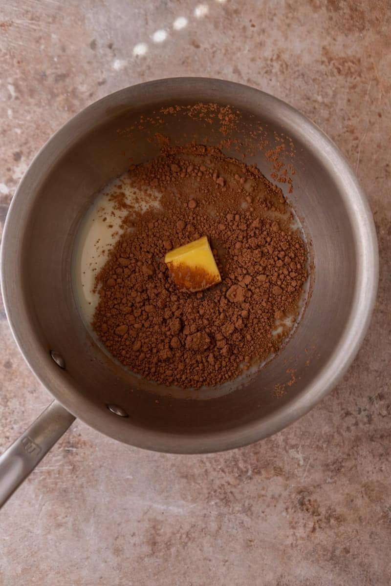 A saucepan with cocoa powder, a pat of butter, and condensed milk before heating