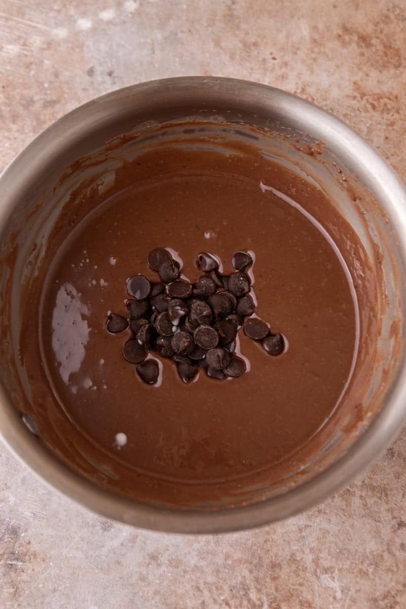 Dark chocolate chips added to the warm chocolate glaze in a saucepan ready to be stirred in
