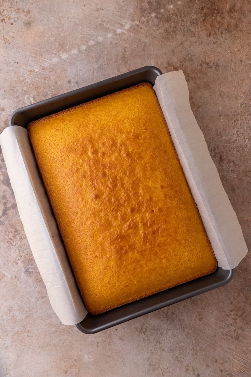 A freshly baked golden orange cake cooling in a parchment-lined 9x13 pan
