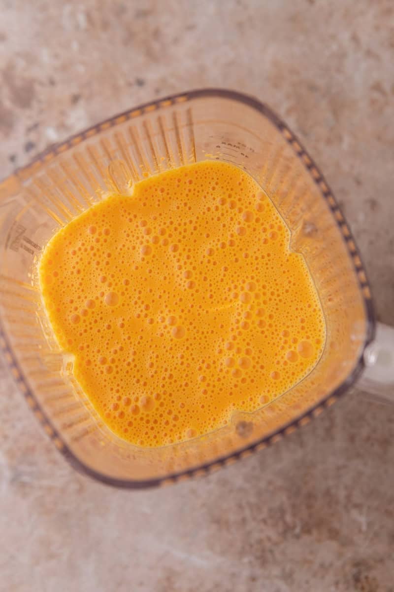 Bright orange blended batter in a blender viewed from above with small air bubbles on the surface