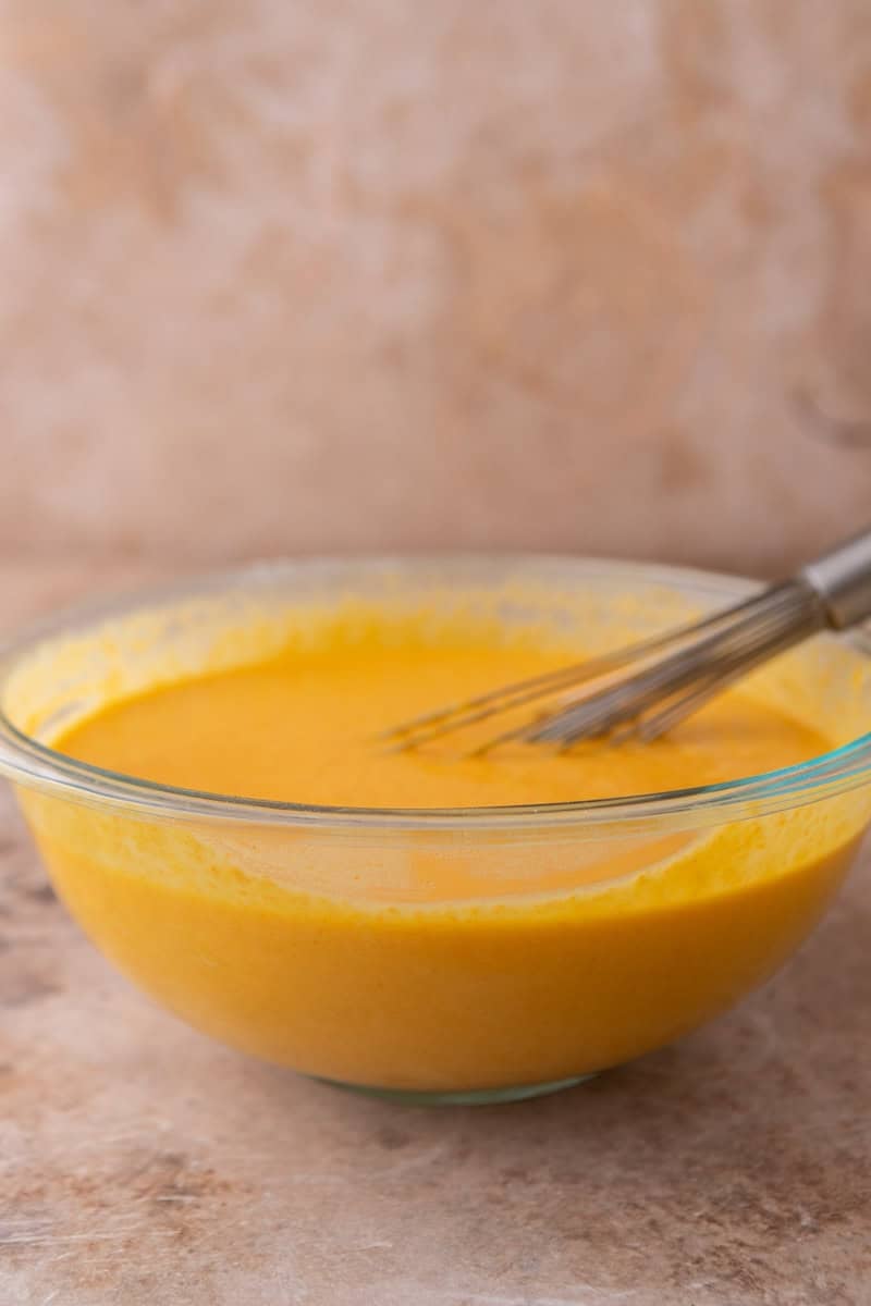 Smooth orange cake batter in a glass mixing bowl with a whisk resting inside