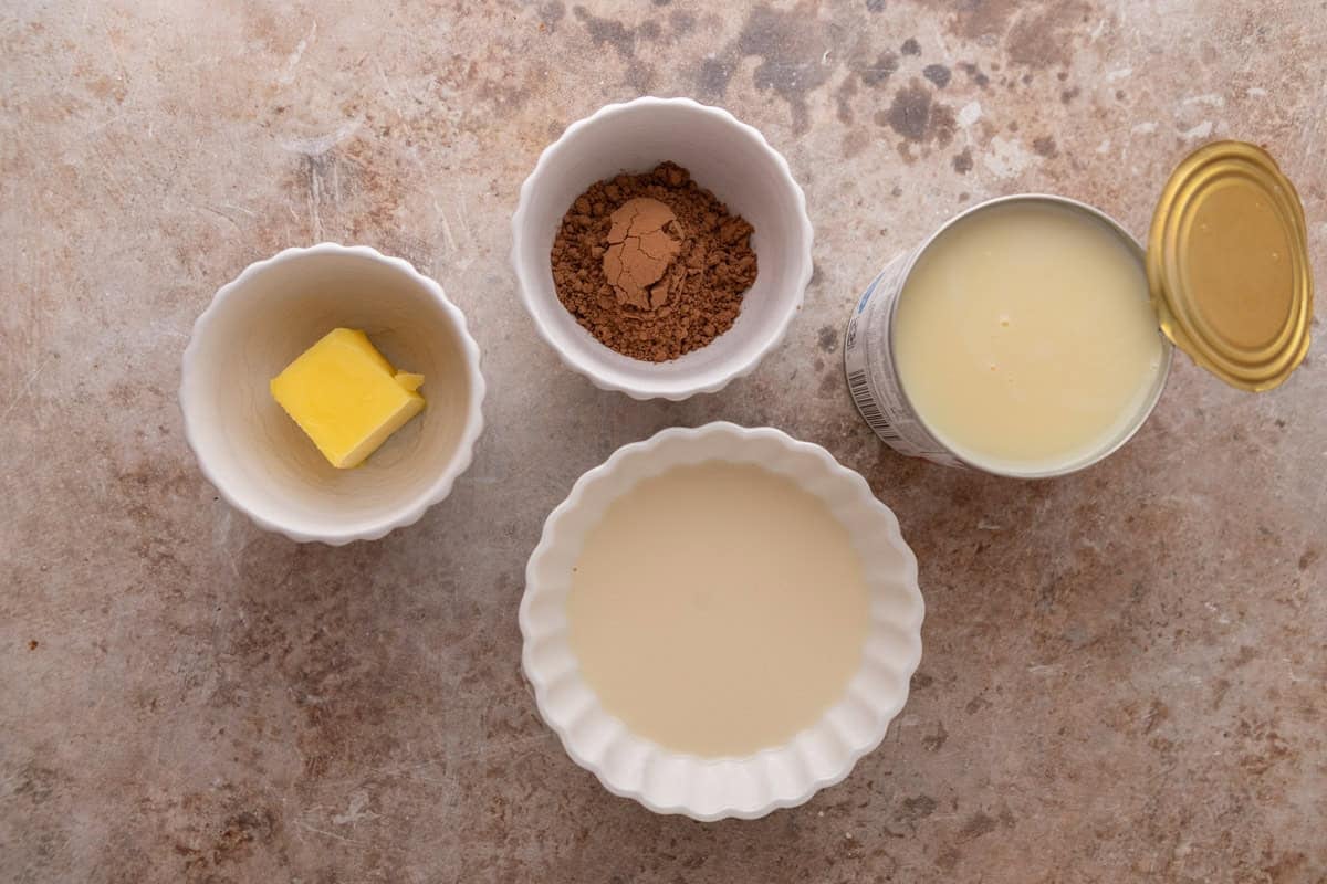 Chocolate glaze ingredients including butter, cocoa powder, evaporated milk, and an open can of sweetened condensed milk