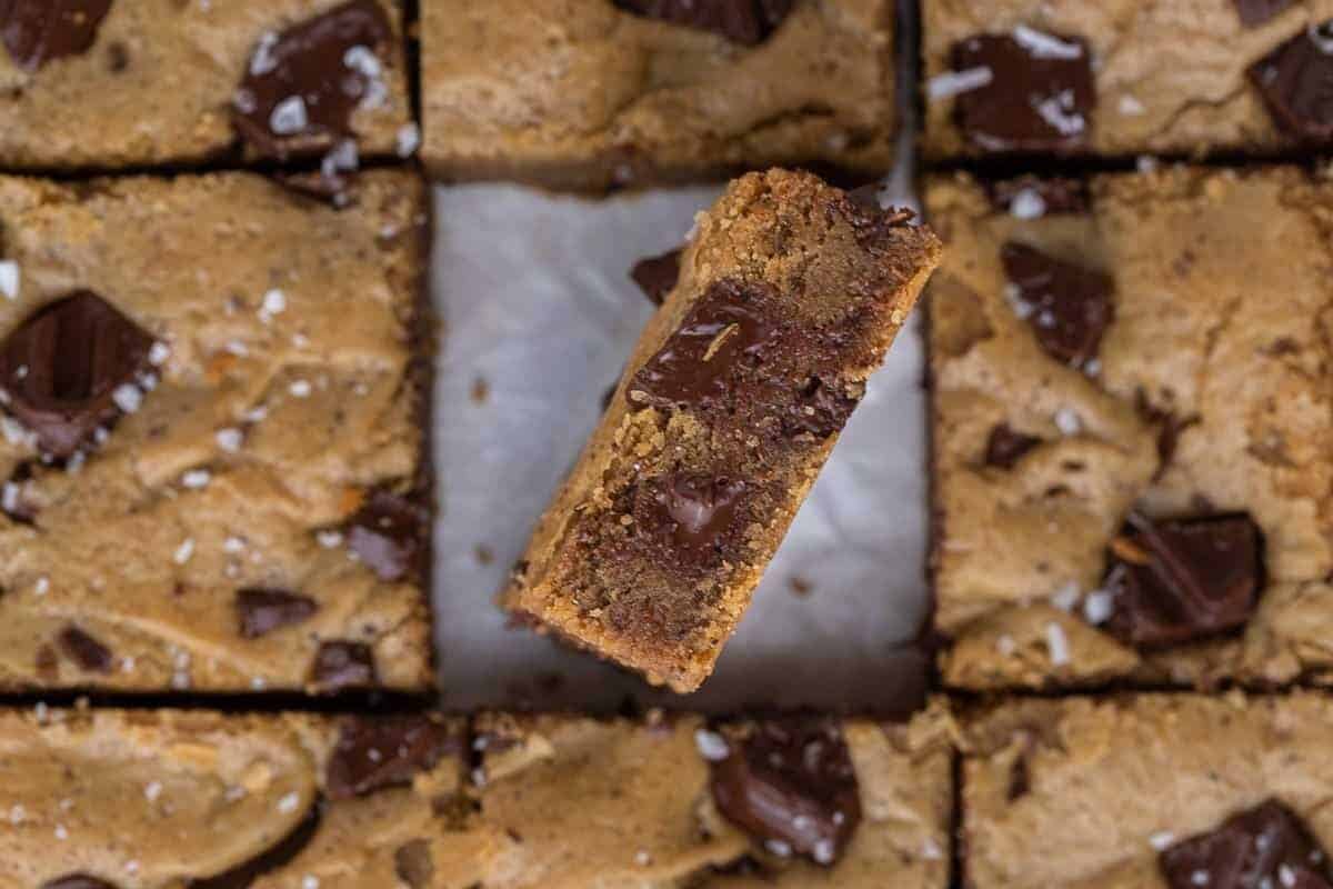 Overhead view of brown butter chocolate chip blondies sliced into squares with one piece tilted to show the chewy fudgy interior with melted chocolate chunks