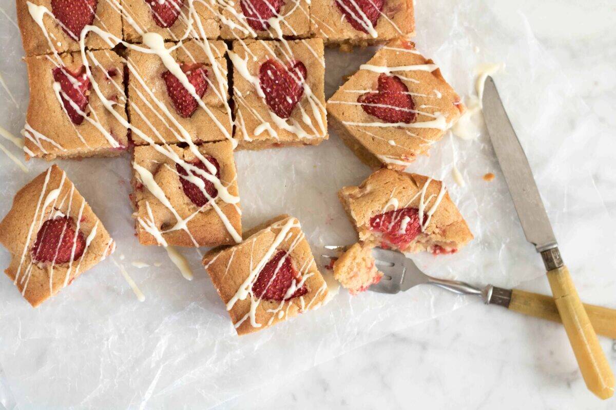 Brown butter strawberry blondies drizzled with white chocolate on parchment paper with fresh strawberry halves baked into each square