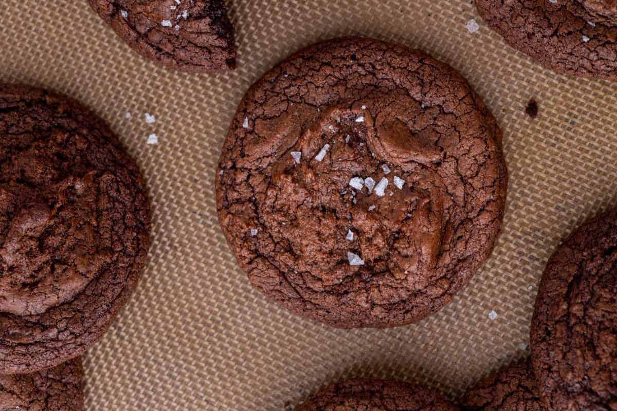 Overhead view of fudgy brownie cookies with crinkly tops and flaky sea salt on a silicone baking mat