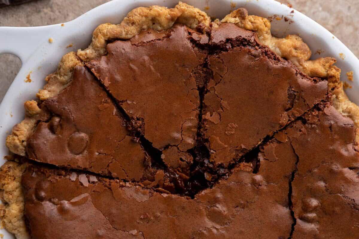 Overhead view of a brownie pie in a white pie dish with a golden pie crust and fudgy chocolate brownie filling sliced into triangular pieces