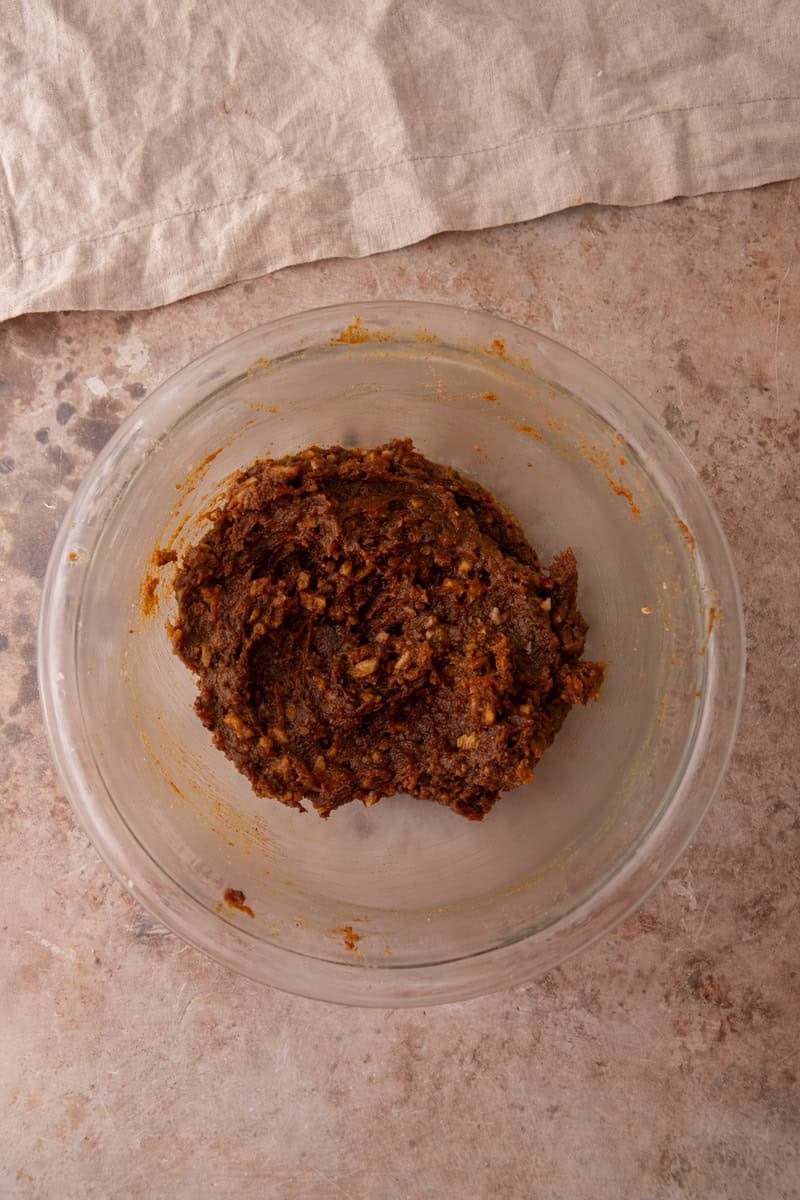Carrot cake cinnamon roll filling mixed together in a glass bowl, showing a thick dark brown paste with walnut pieces