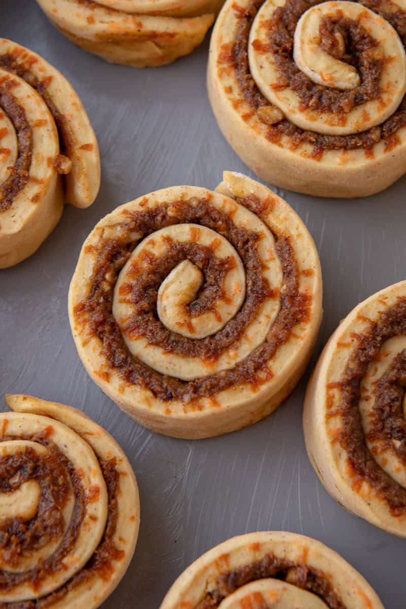 Unbaked carrot cake cinnamon rolls showing the spiral swirl pattern of brioche dough and spiced brown sugar filling