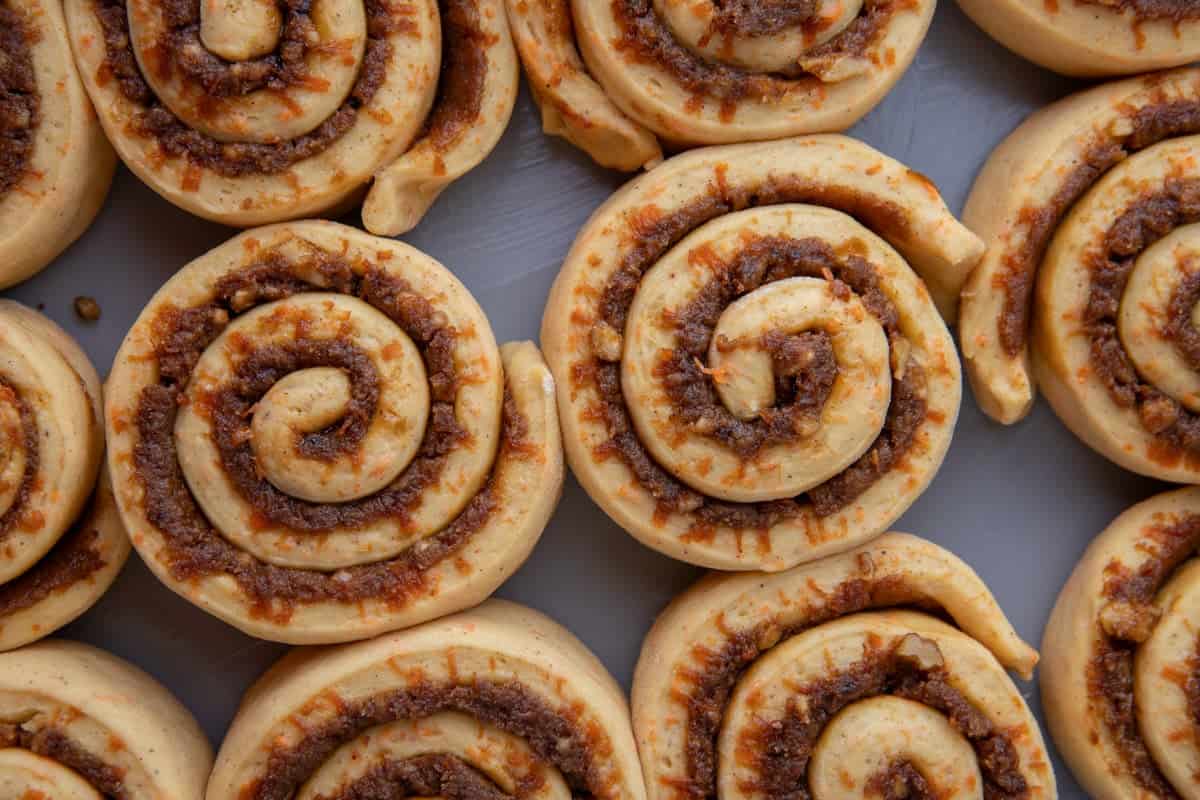 Twelve unbaked carrot cake cinnamon rolls arranged in a baking pan showing the swirl pattern before rising