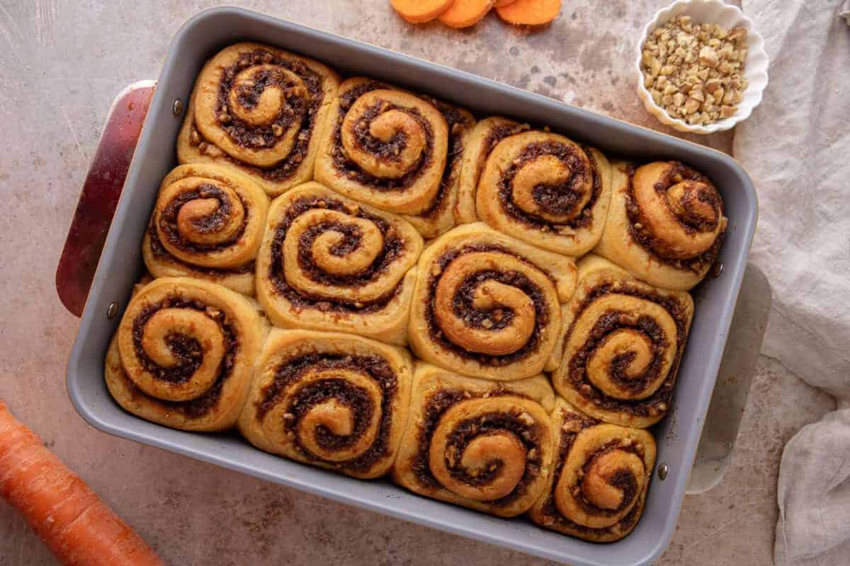Twelve freshly baked rolls in a 9x13 baking pan with golden tops and visible cinnamon swirls, unfrosted